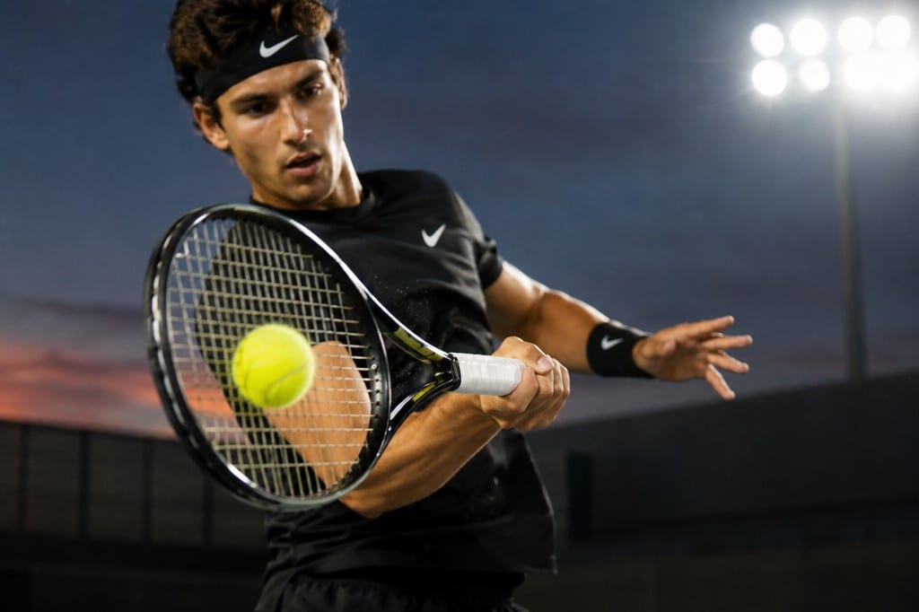 Professional tennis player executing a topspin forehand swing at night under stadium lights